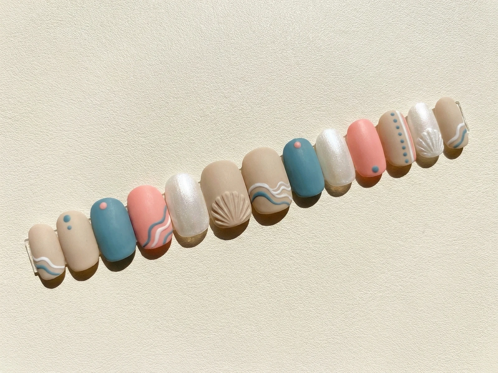 Twelve coordinated coastal-color nail tips arranged on a salon board